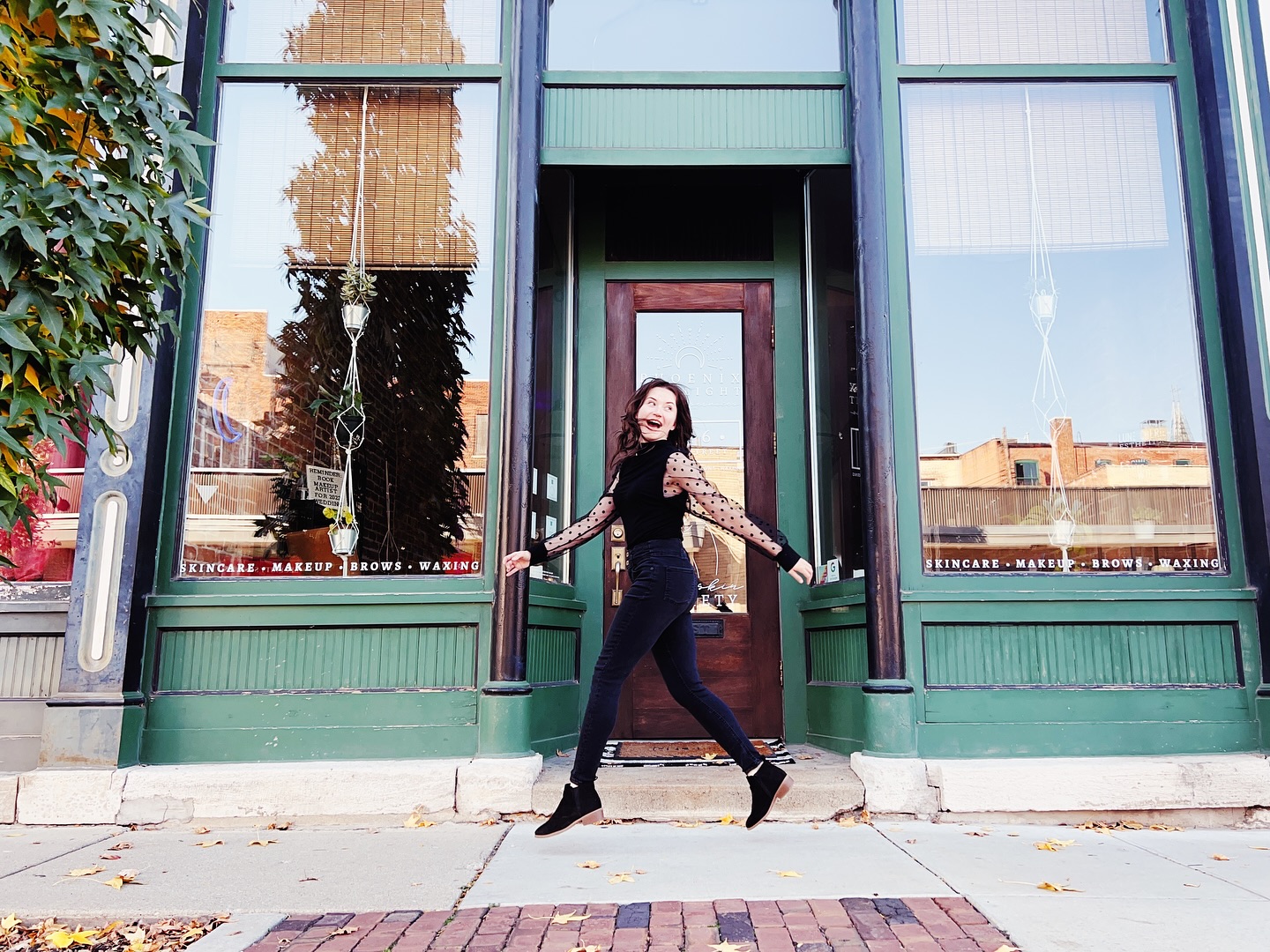Woman joyfully leaping in front of a green skincare and makeup storefront.