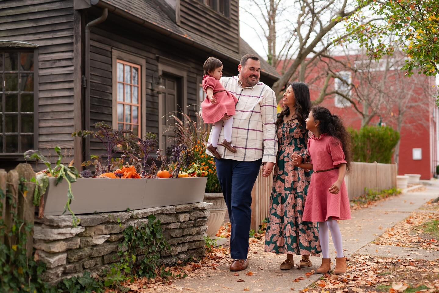 A family of four walking happily down a sidewalk in the fall.