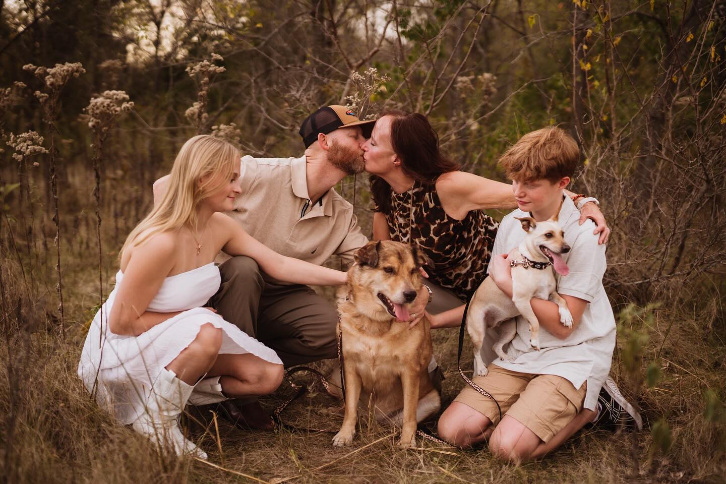 A family of four and their two dogs posing together in a rustic field.