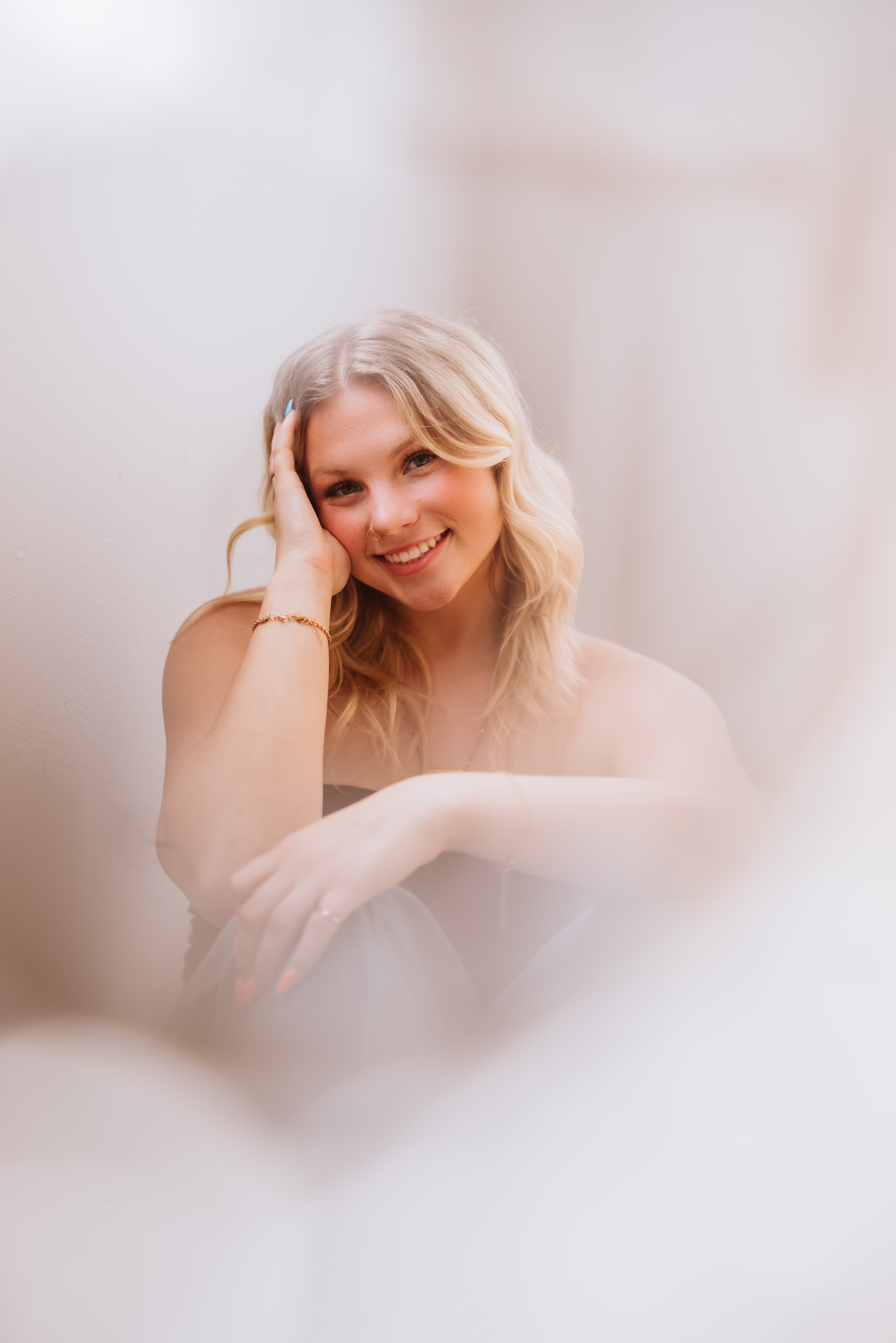 Dreamy close-up portrait of a smiling blonde senior with hand resting on her cheek.