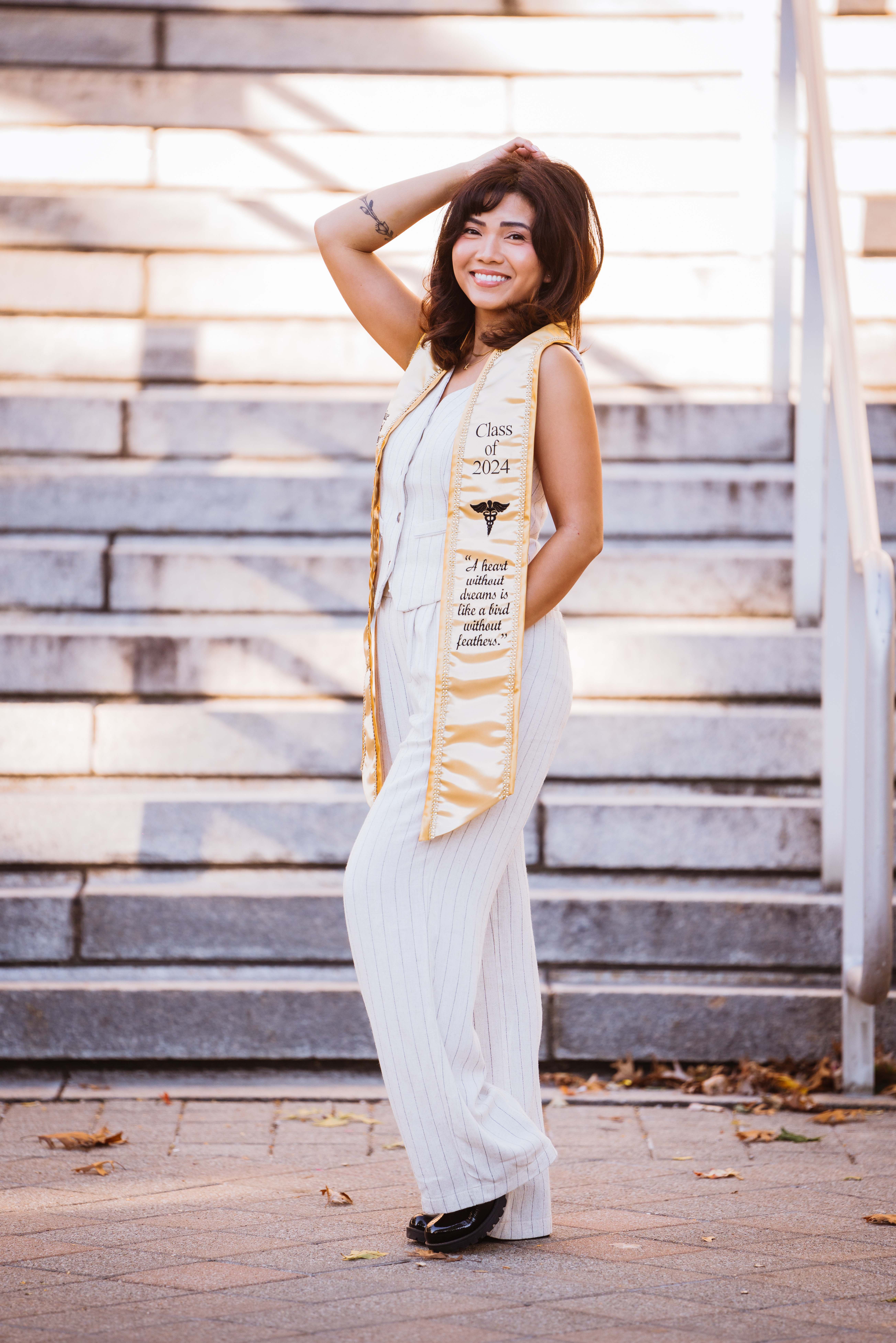 Senior in a white pinstripe suit and 'Class of 2024' sash posing on steps.