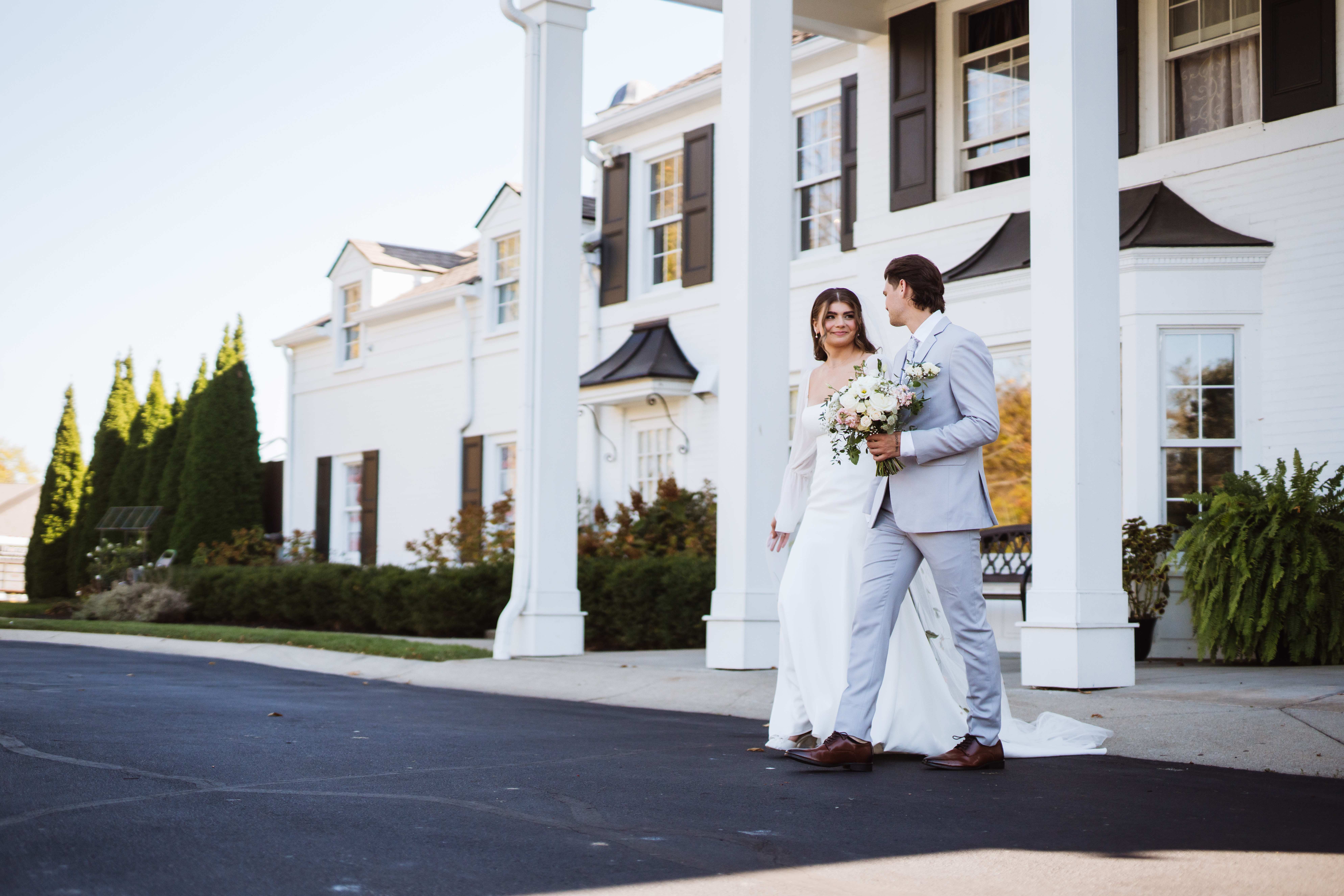 Bride and groom walking together in front of a grand white colonial building.