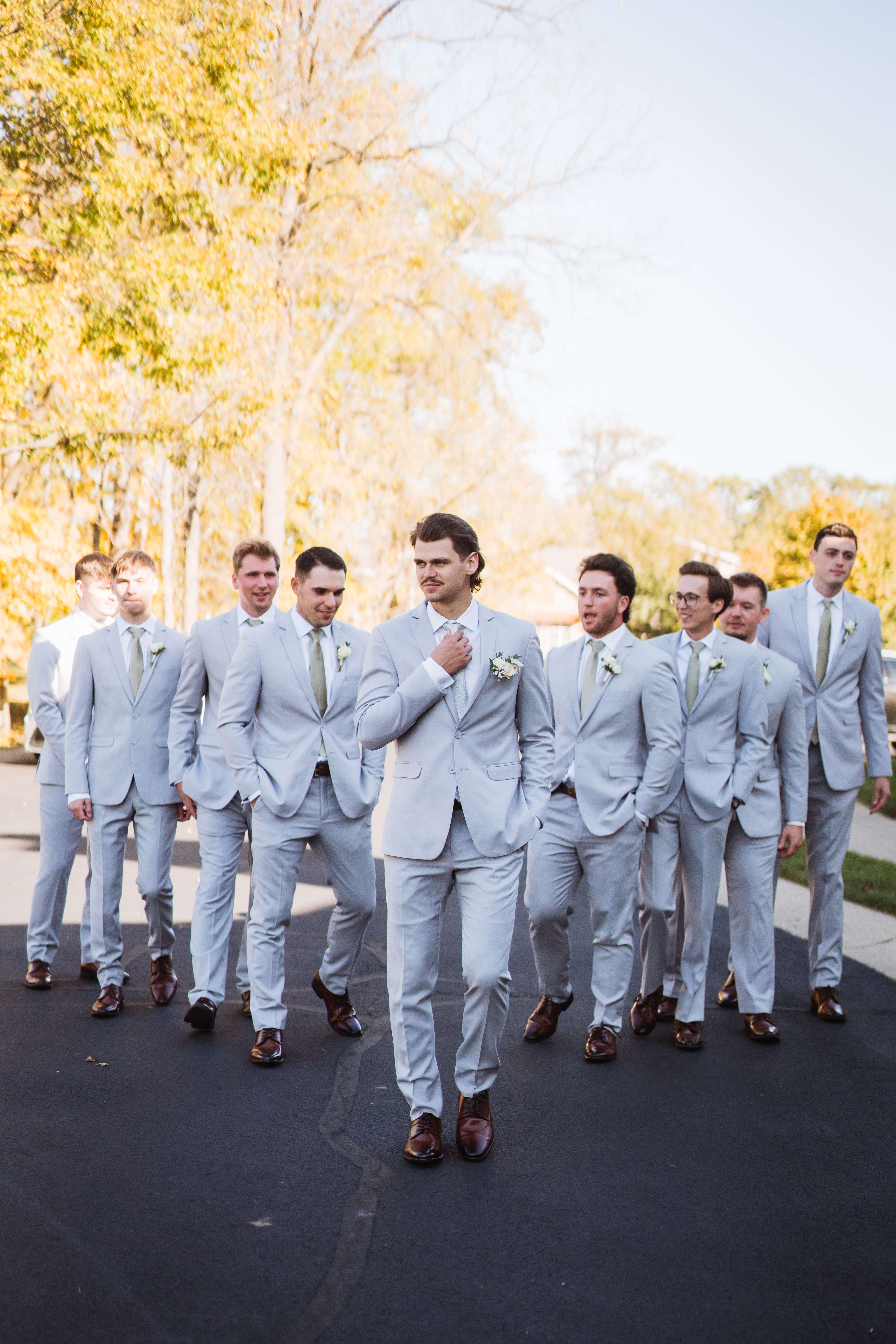 Groom and groomsmen in light grey suits walking confidently down a path.